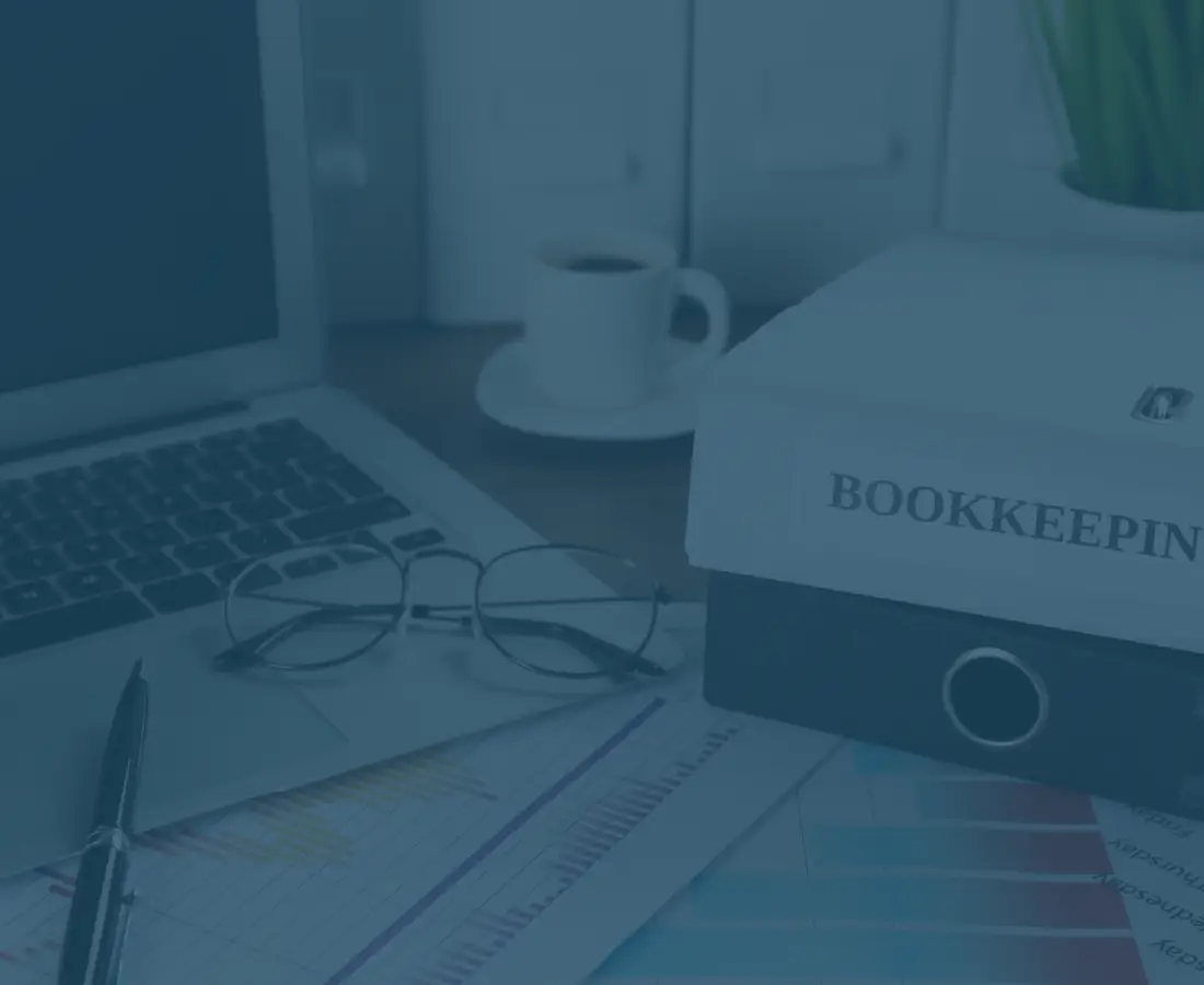A workspace with a laptop, glasses, coffee cup, and a book titled 'BOOKKEEP'.