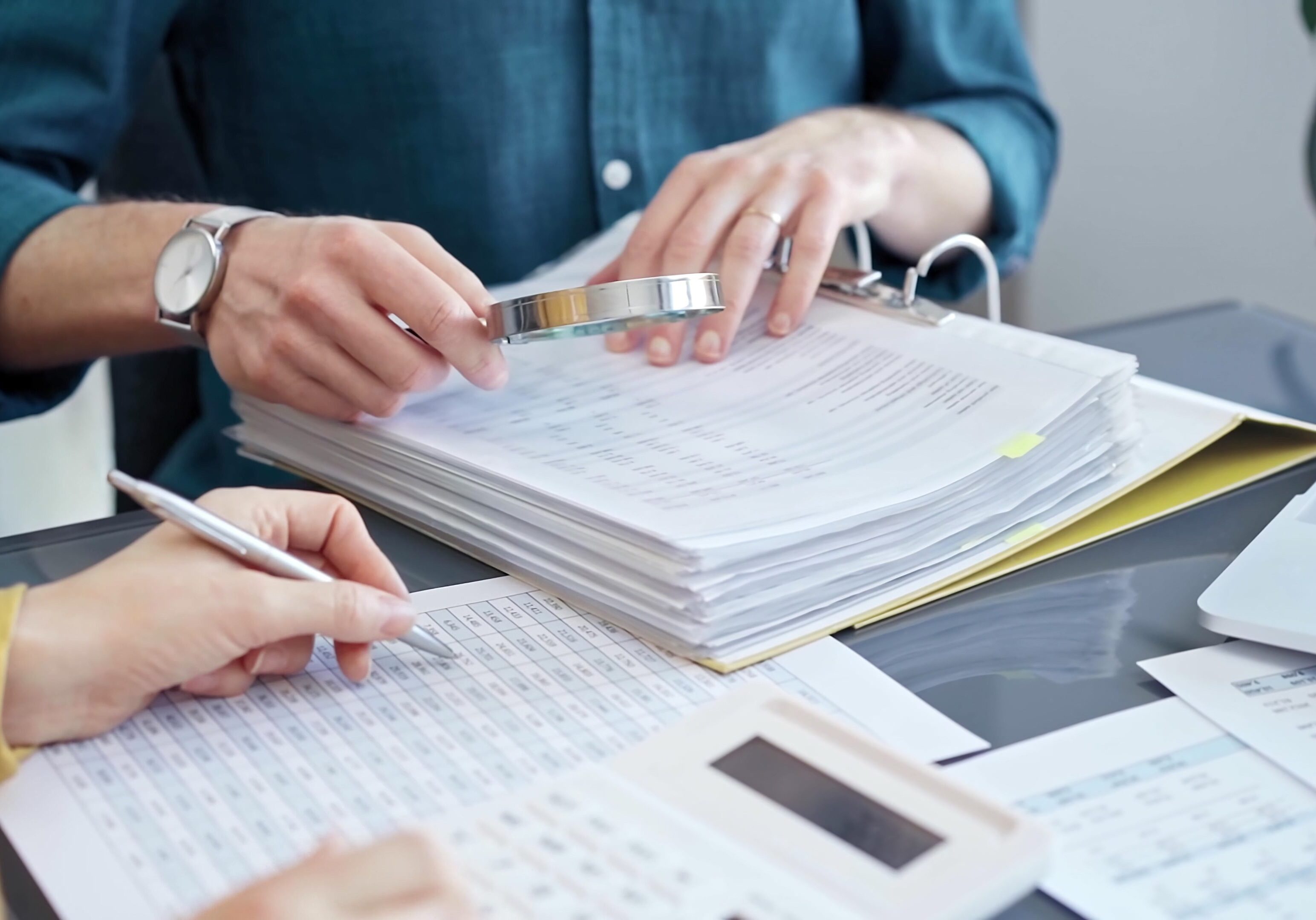 Two people reviewing documents with a calculator and pen.